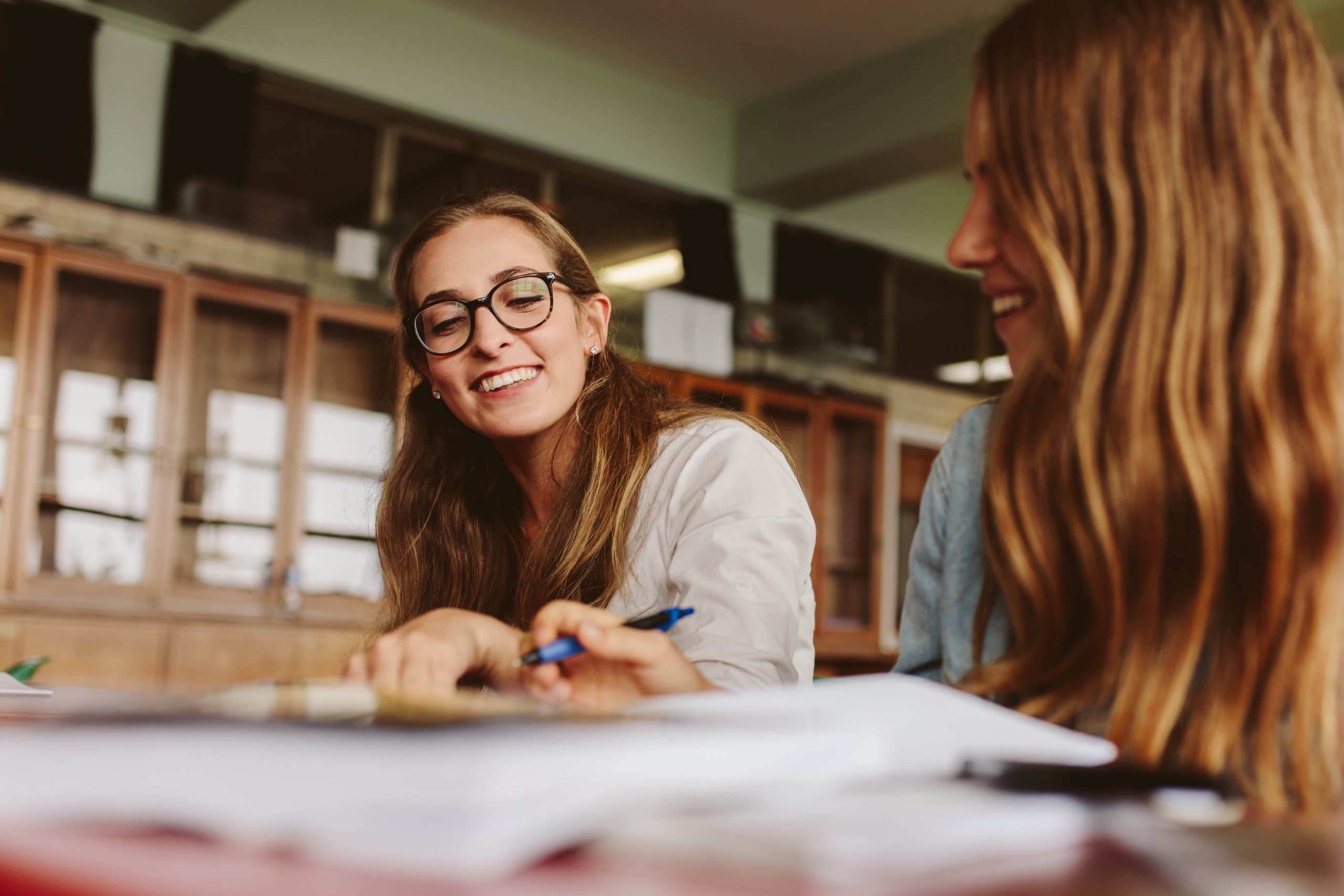 Leende ung lärare som hjälper en kvinnlig student under hennes lektion. Glad föreläsare som hjälper en student.