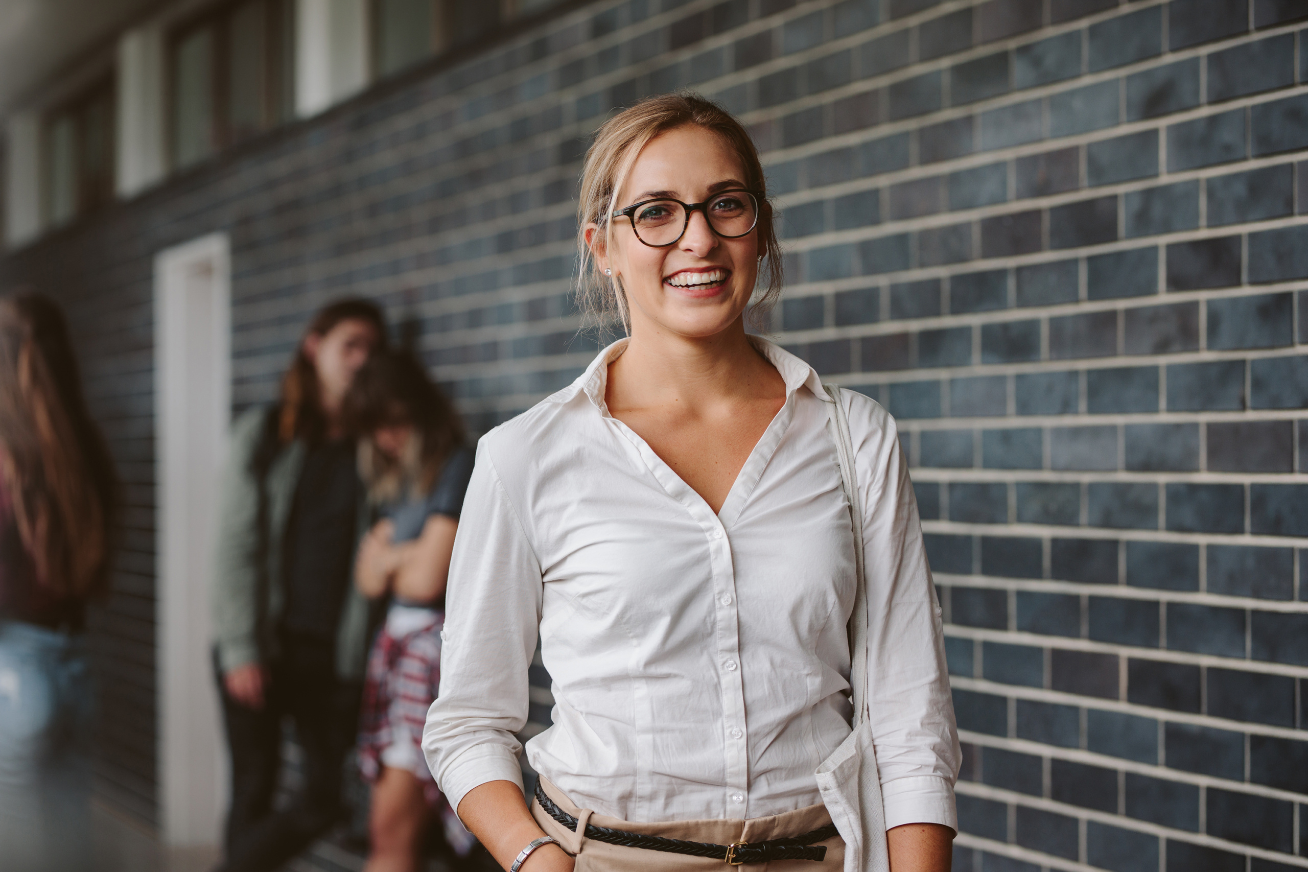 Porträtt av en kvinnlig lärare som står i en skolkorridor med elever bakom sig